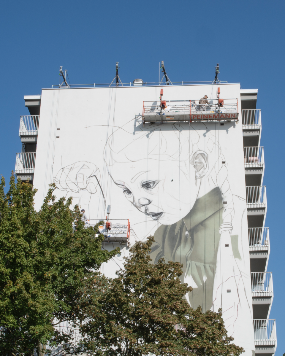Graffiti artiest Smug aan het werk op hoogwerker tijdens groot mural project in Geleen